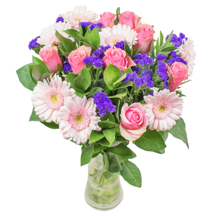 A meticulously arranged bouquet, reminiscent of the landscapes surrounding Tadworth, sits in a clear, slender vase against a simple, clean backdrop. At its heart are 7-9 pink roses-some elegantly furled, others just beginning to open-celebrating the classic spiral of each bloom. These are entwined with 5-7 pale pink gerbera daisies, each displaying a radiant face and slightly lighter centre, evoking morning light across Headley Heath. Vibrant purple statice, their clustered papery petals adding texture and depth, introduces a lively splash that accentuates the predominant pinks. Rich, dark green foliage adds volume, reminiscent of Tadworth's tree-lined lanes and lush public gardens. Through the clear water-filled vase, the freshness of each stem is visible, carrying the promise of local same-day delivery from Flowers Tadworth. Perfect for Tadworth occasions-be it a birthday along Station Approach, an anniversary, Mother's Day, or a beautiful gesture to add grace to home or office-the bouquet conveys joy, celebration, and affection, celebrating the artistry and personal touch of your community florist.